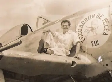 Fotografía histórica en blanco y negro de un miembro del Escuadrón 201, presuntamente un mecánico de aviación, sonriendo mientras posa sentado sobre un avión Republic P-47D Thunderbolt en Filipinas durante la Segunda Guerra Mundial. El fuselaje muestra claramente el emblema del 