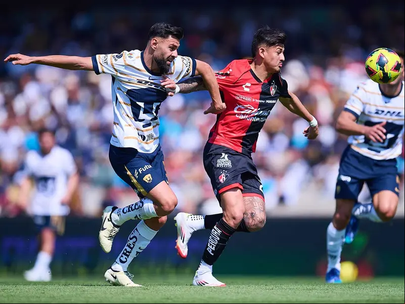 Jugadores de Pumas y Atlas corriendo tras el balón.